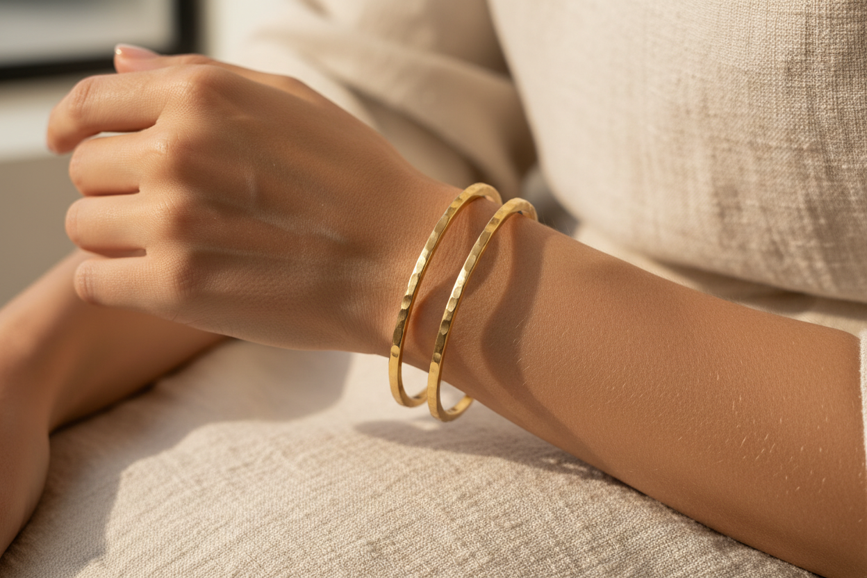 Close-up of a hand wearing a gold bangle on a neutral background