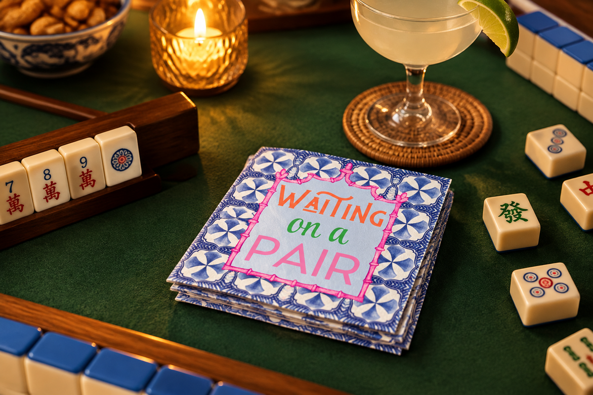 Fabuplates Waiting on a Pair blue and white tile mahjong cocktail napkins on a green mahjong table with tiles, a candle and a cocktail