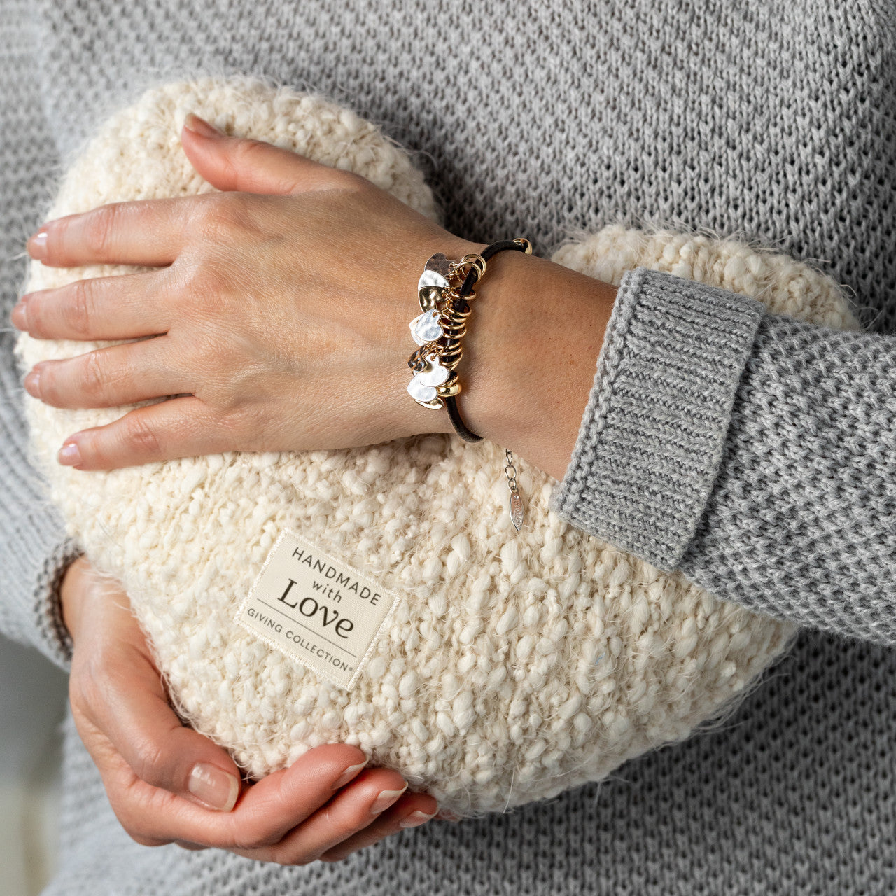 Person holding a textured white pillow with 'Handmade with Love' label, wearing a gray sweater and gold bracelet.