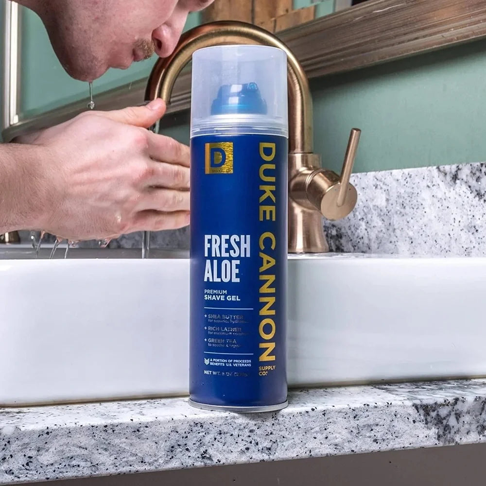 Duke Cannon Fresh Aloe shave gel can on a bathroom counter with a person washing hands in the background.