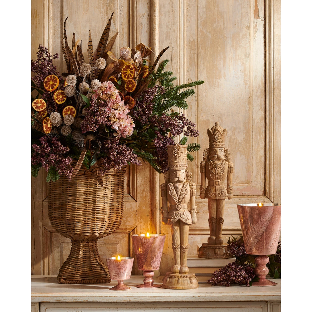 2 natural colored nutcrackers on a mantel with florals and candles surrounding them 