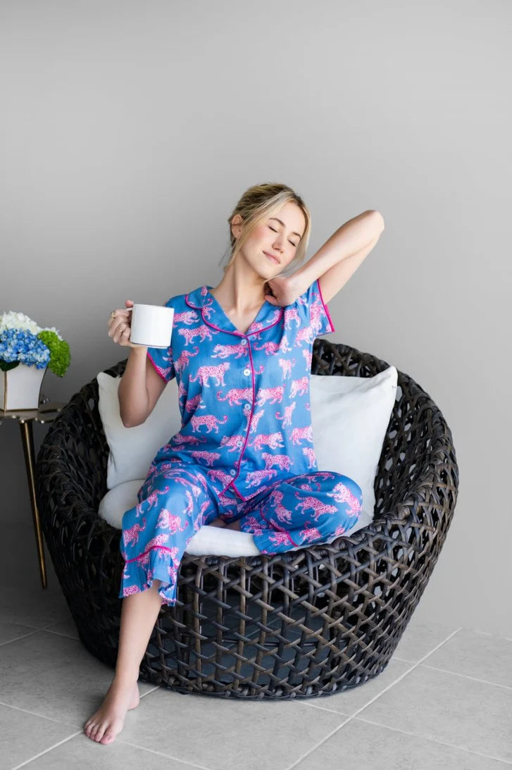 woman in blue and pink leopard print pajamas in a chair holding coffee on a white background